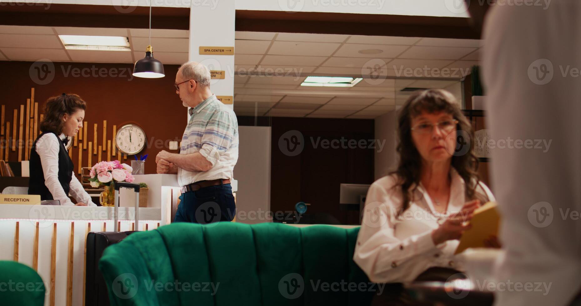 Elderly adult registering in hotel lobby after arriving on international vacation, discussing with front desk staff about room reservation. Concierge offering excellent services to customer. photo