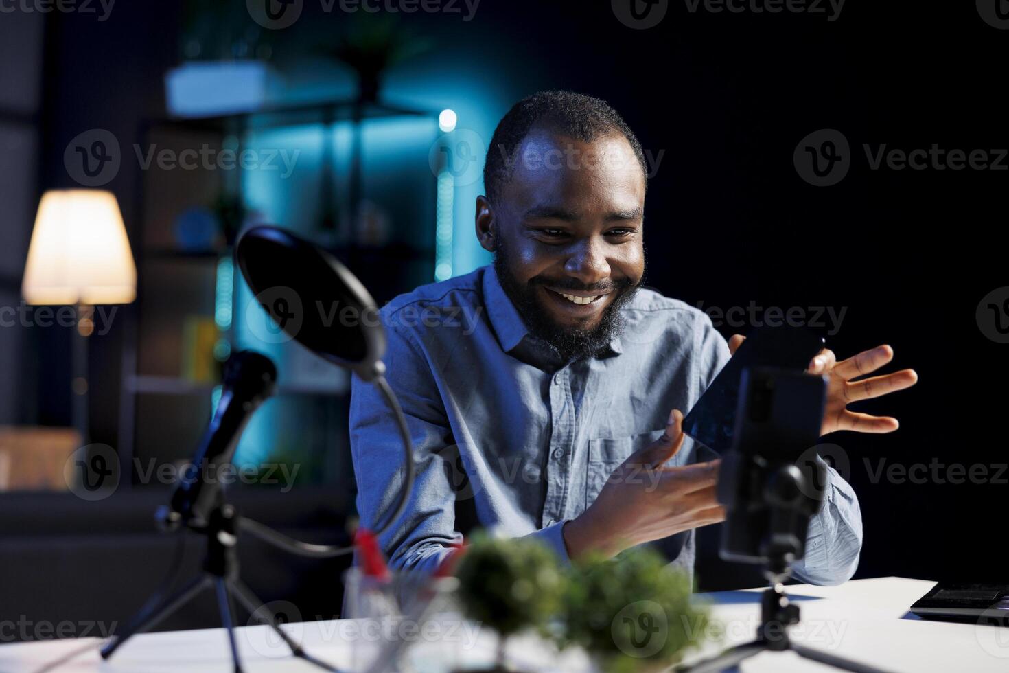 African american internet show host using smartphone camera to film content about best cellphones on the market. Media star recording mobile phone review for tech enthusiasts photo