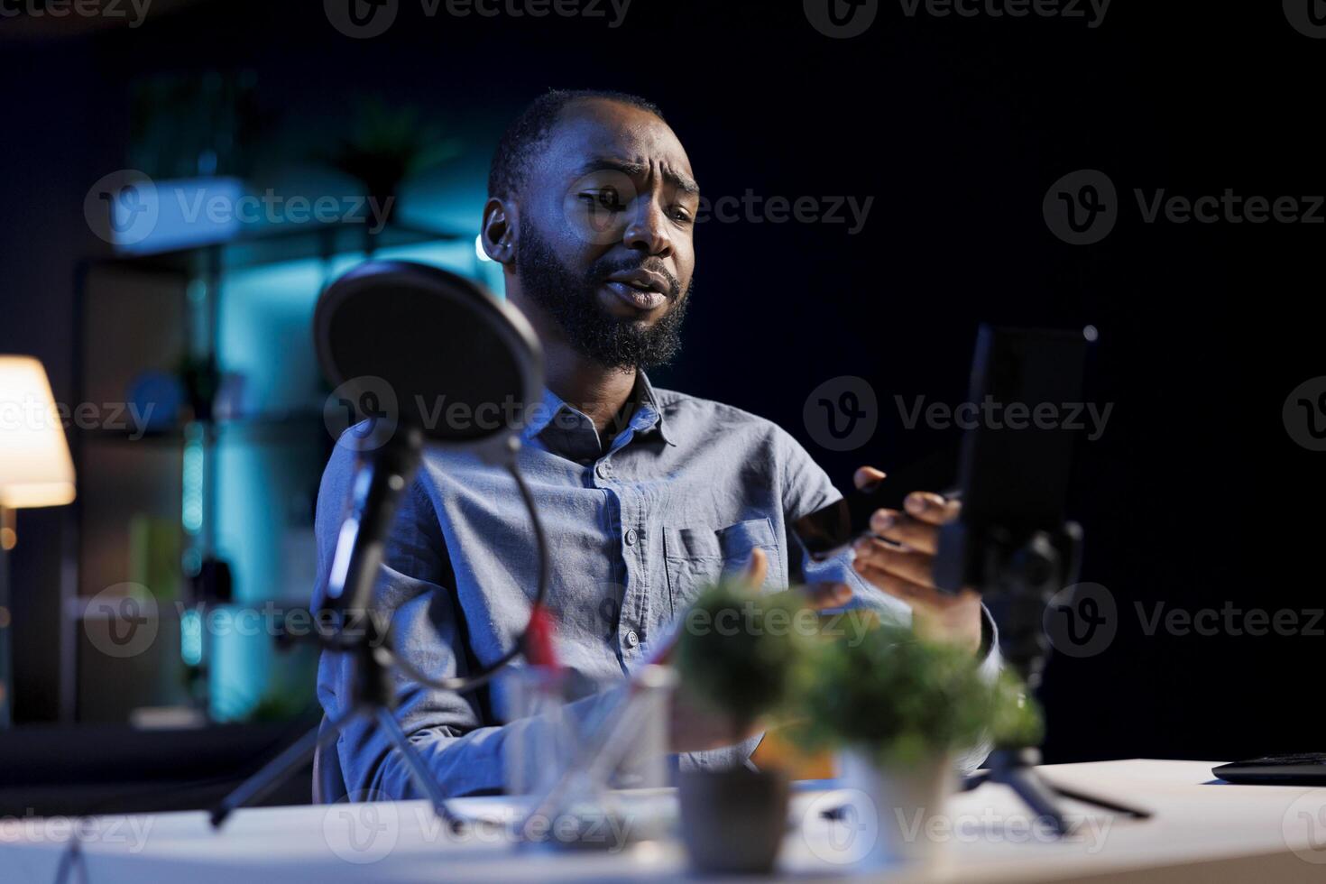 African american internet show host using smartphone camera on phone holder to film content about best mobile phone releases of the year. Online star recording newly launched cellphone review photo