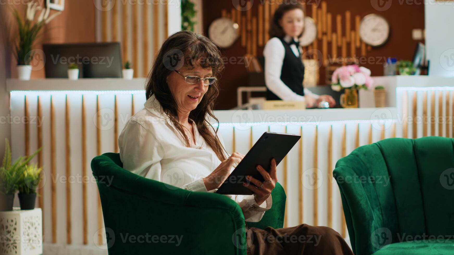 Hotel guest using modern device in lounge area, waiting for check in and navigating on online webpage. Elderly woman browsing internet after arriving at five star holiday resort. Handheld shot. photo