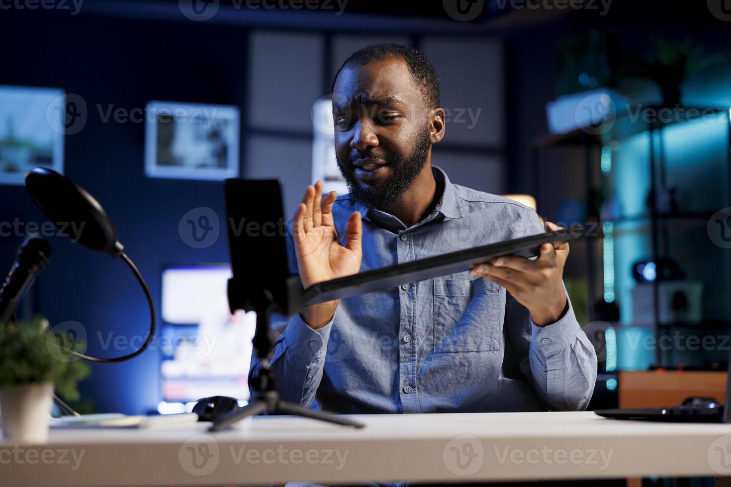 Online star using smartphone on selfie stick to film reviews of various electronics, unboxing them and presenting features to viewers. Man showcasing products for his internet channel photo