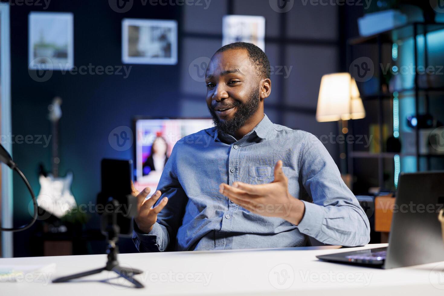 Mobile phone used for recording cheerful entertainer chatting with online audience, filming in home studio. Media star discussing with fans during live broadcast stream filmed with cellphone photo