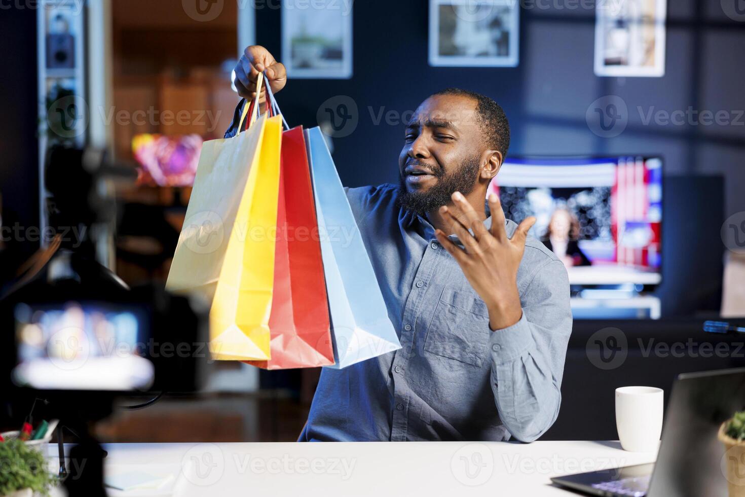 Blogger doing shopping haul, holding colorful bags in hand, showing subscribers purchases he recently got. Internet star presenting fanbase new acquisitions, filming himself in apartment photo