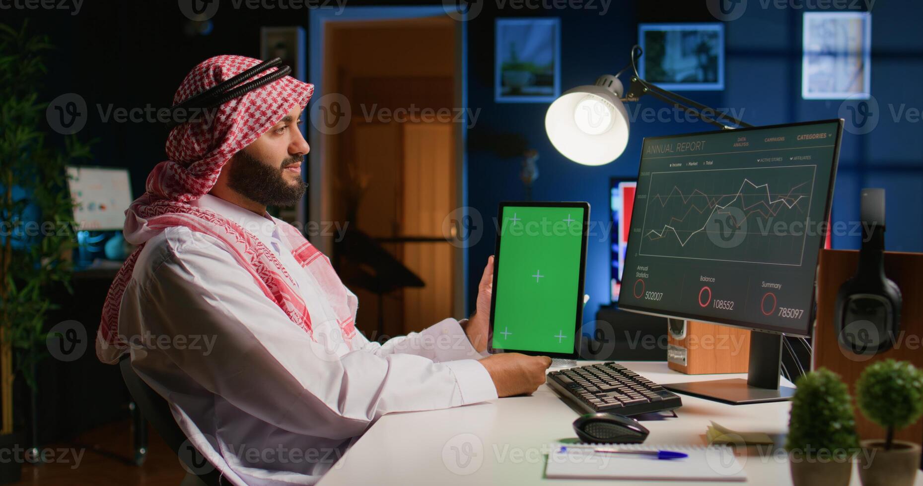 musulmán trabajador en Departamento oficina sostiene croma llave tableta, comprobación cruzada datos en eso con negocio reporte gráficos en computadora. sonriente empresario con Bosquejo digital dispositivo en mano realiza trabajo Tareas foto