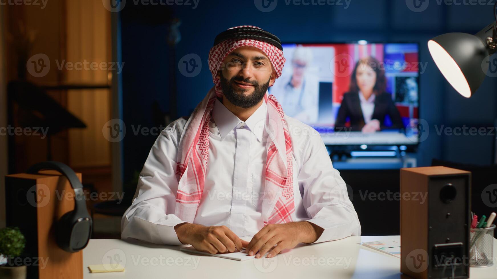 Cheerful Arab man paying attention in elearning seminar teleconference with teacher. Middle Eastern student in online videocall greeting tutor, listening to lesson while writing down homework tasks photo