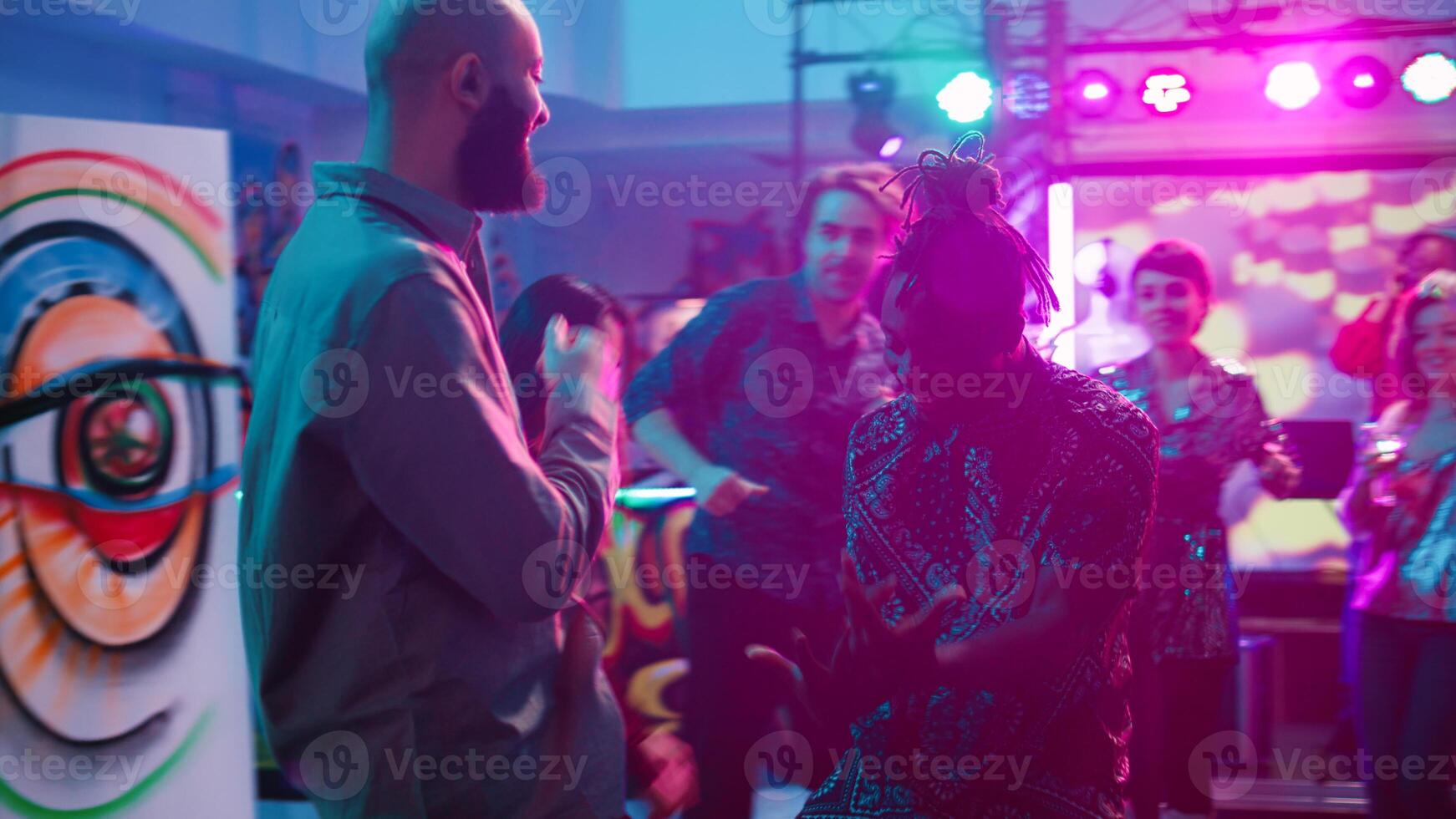 Happy people partying together on music, enjoying night out at underground party. Group of smiling friends dancing on electronic music having fun at discotheque with spotlights. Handheld shot. photo