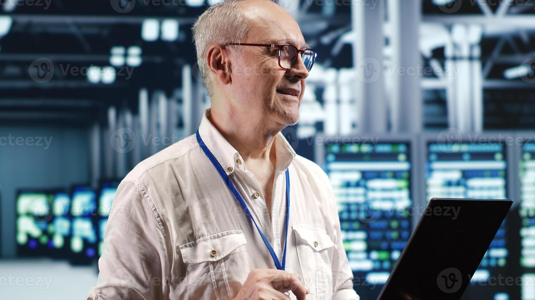 Elderly professional navigating network of server gadgets in industrial hub. Technical support specialist with laptop doing optimizations and maintenance in data center, preventing system hazards photo