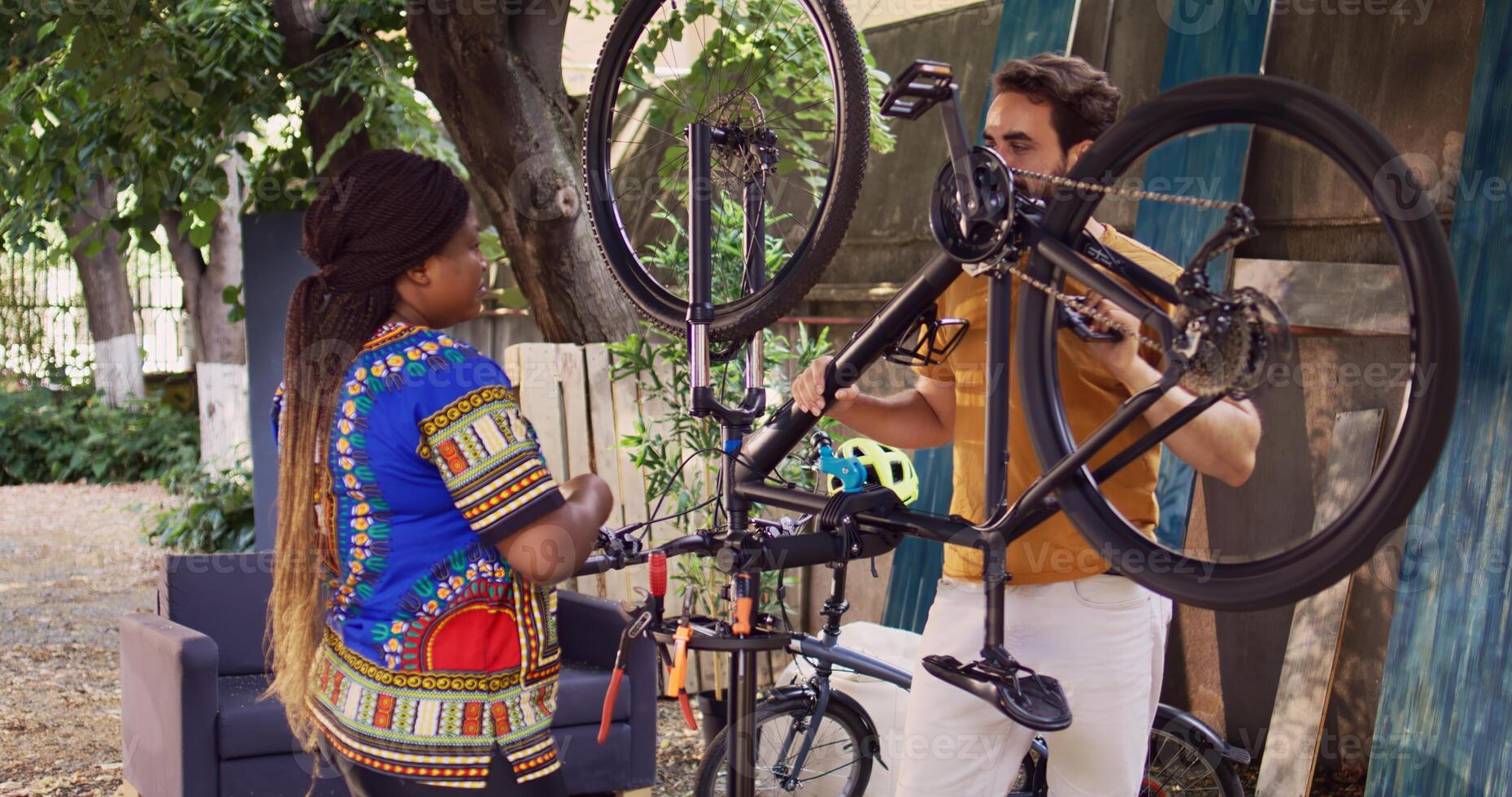 Girlfriend and boyfriend fixing bike tire with specialised tools in home yard as yearly maintenance. Athletic interracial couple discussing on best way to repair and maintain bicycle. photo