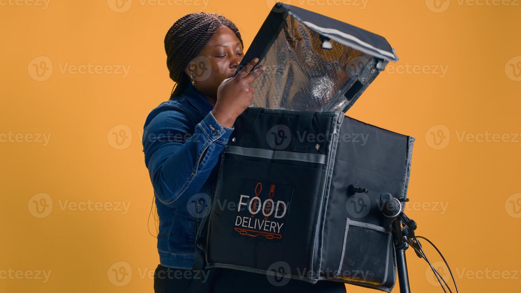 africano americano mujer coleccionar para llevar desde comida entrega bolso para cliente. profesional mensajero proporciona rápido y confiable cliente Servicio por entregando delicioso eliminar comidas con bicicleta. foto