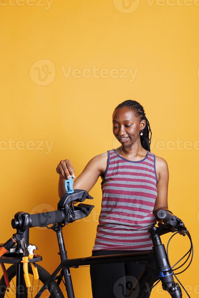 Youthful female cyclist of african american ethnicity inspects broken bicycle components with tools. Black woman expertly and precisely arranging repair stand for bike adjustments and maintenance. photo