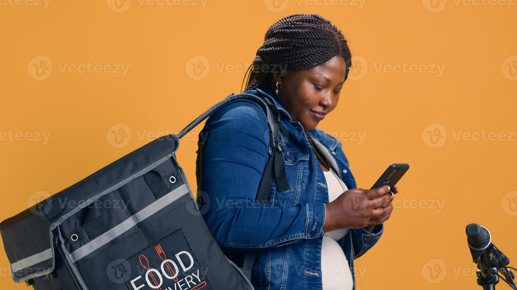 Before riding for food delivery service an enthusiastic delivery woman uses her smartphone to message coworkers. African American courier scanning a mobile app for parcels to deliver on-demand. photo