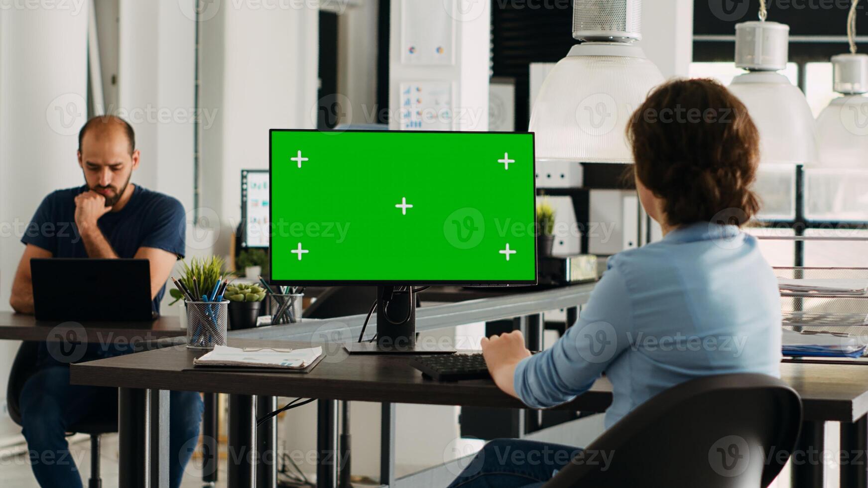 Businesswoman looking at greenscreen display to work on agency tasks, employee analyzing isolated chromakey template at desktop. Person working with copyspace, problem solving. photo