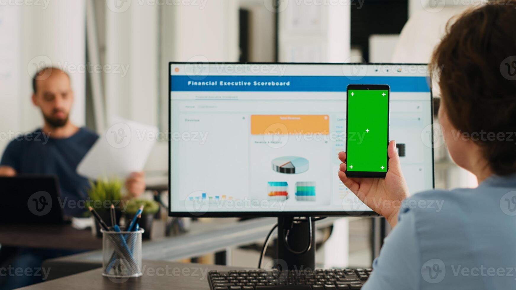 Adult holding phone with greenscreen in coworking space at office. Businesswoman working with smartphone showing isolated mockup template, analyzing chromakey layout on gadget. Tripod shot. photo