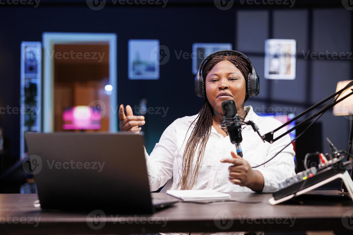 Black woman influencer who talks about emerging trends while creating videos for her internet followers. African lady speaking on a microphone while filming a promotional video wears headphones. photo