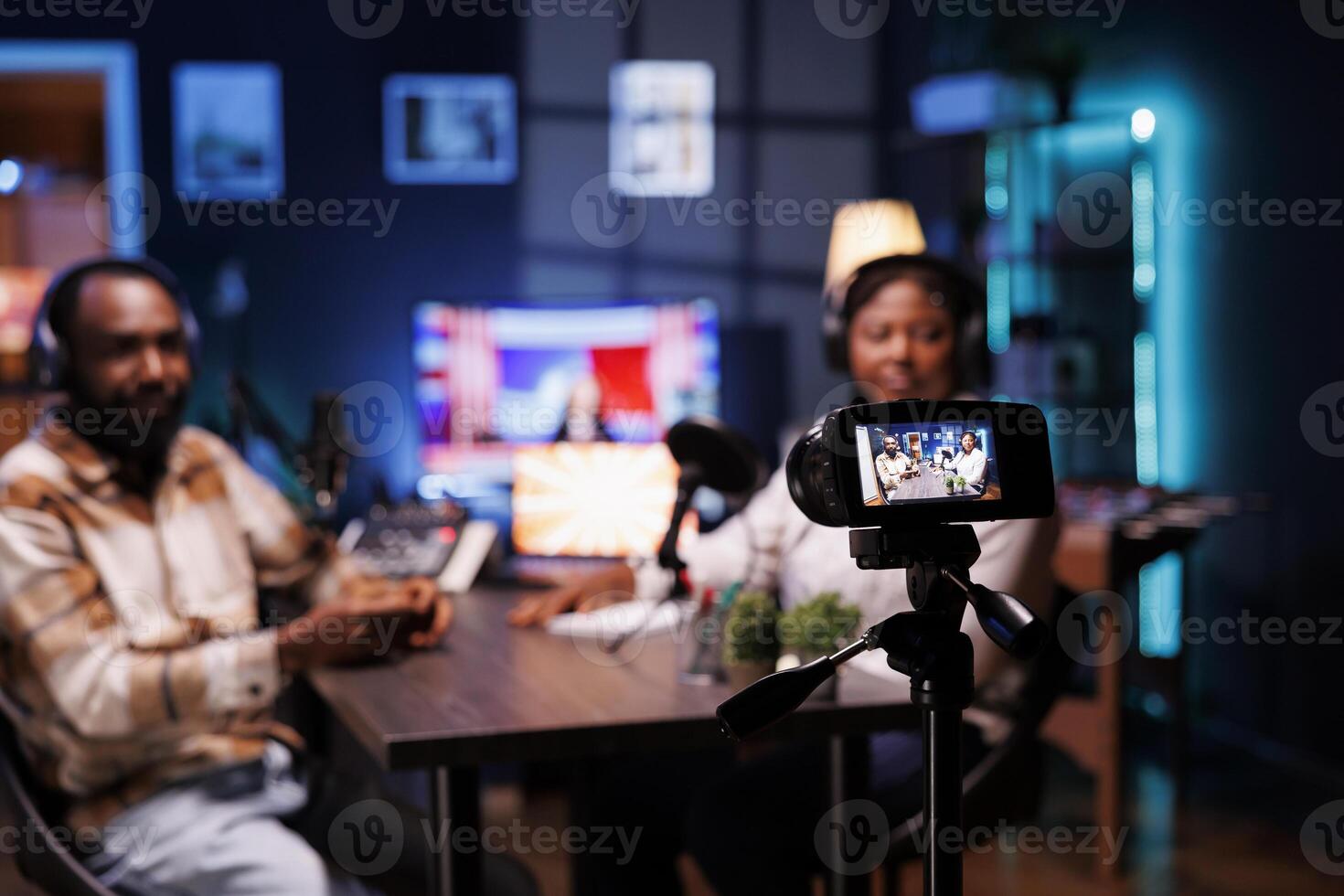 During live broadcast, podcast host records guest sharing engaging story with audience by mounting professional device on a tripod. Camera taking video of bloggers delivering facts in home studio. photo