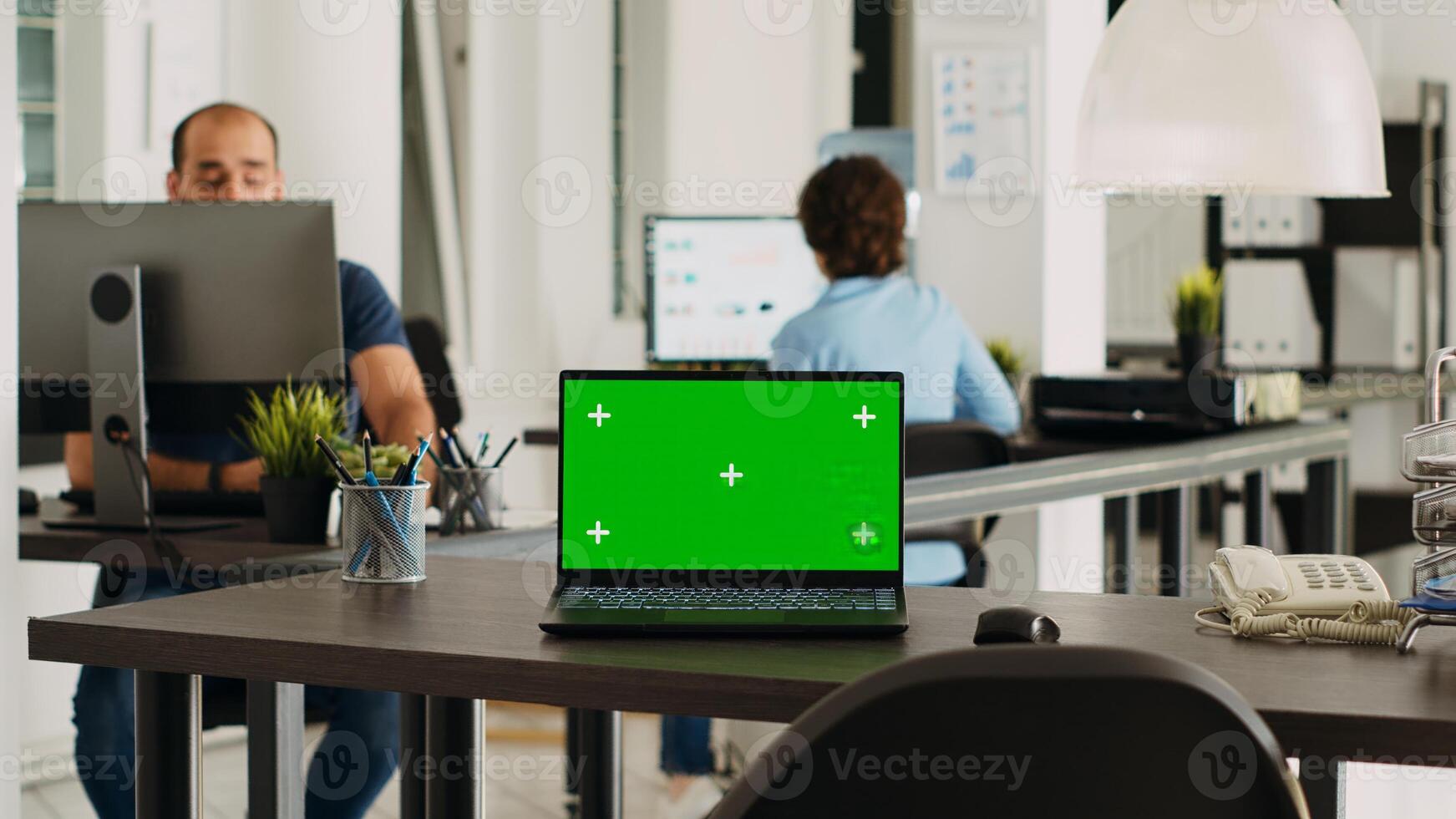 Laptop with greenscreen display on desk in modern startup agency office, wireless computer running isolated mockup copyspace. Empty workstation with chromakey blank device. photo