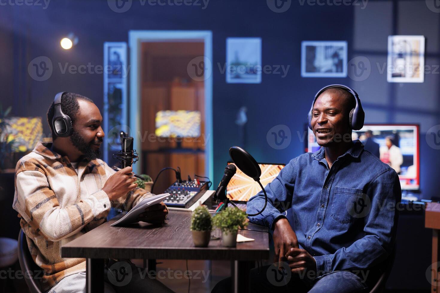 Program host and guest conversing in an elaborate home studio with neon lighting. African american influencers use professional equipment to broadcast a discussion on online podcast episode. photo