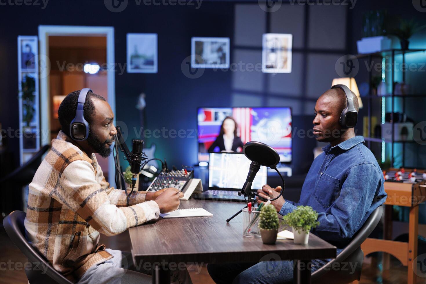 Sitting at table using the audio equipment are two african american men discussing and addressing their online audience. Interviewer asking male influencer questions, recording a radio show at home. photo