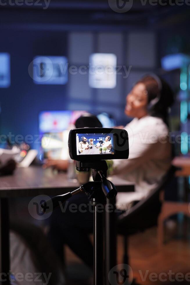 Male and female African American influencers are recording a podcast in neon-lit studio. They are using digital camera to create content for internet video channel and live streaming on social media. photo