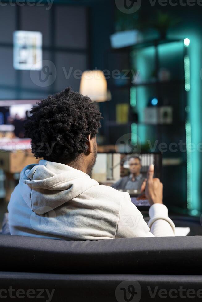 African american job candidate remotely being interviewed via internet videocall by manager. Man answering HR person interview questions during videoconference meeting while staying in apartment photo