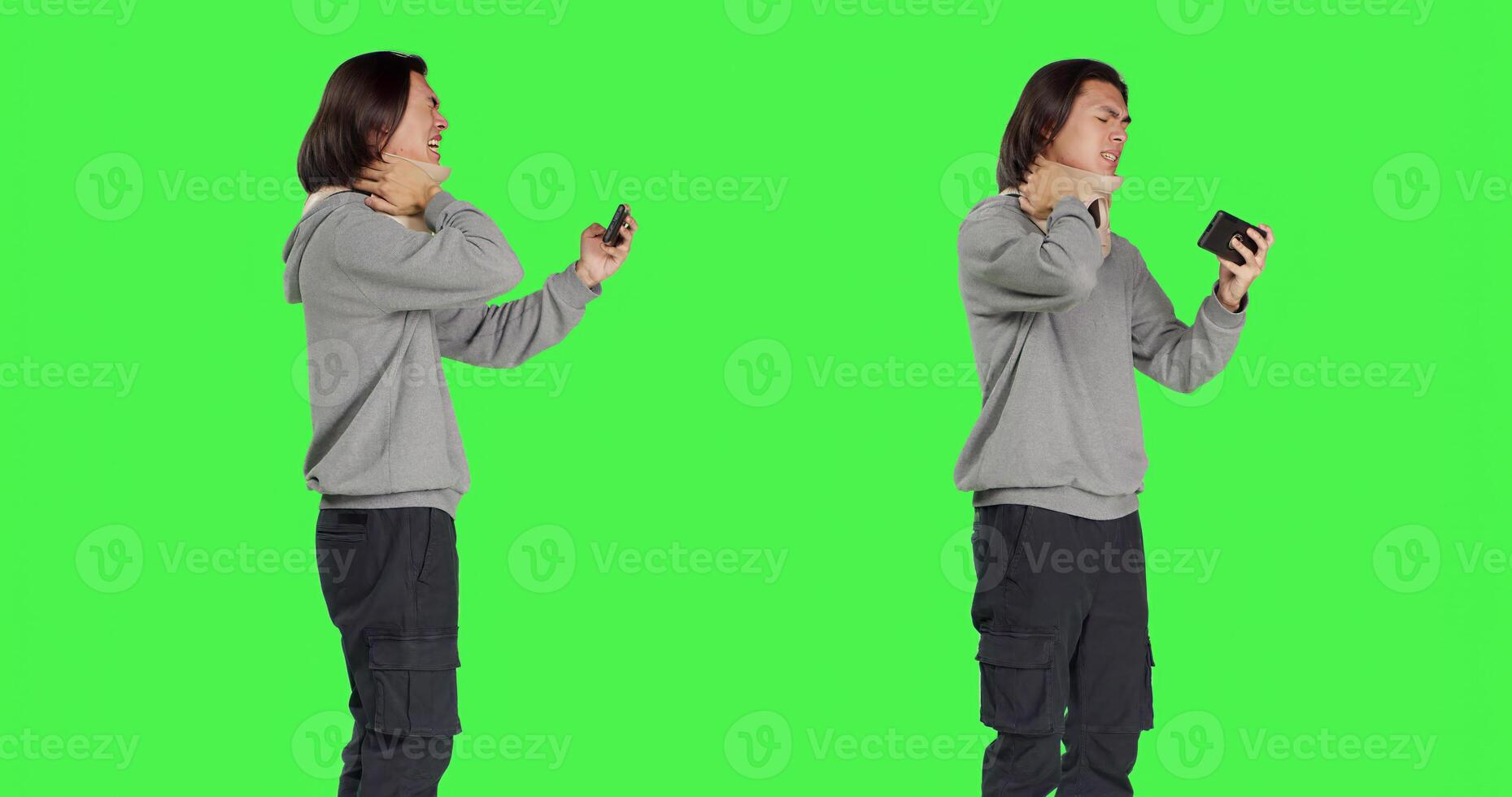 Asian man filming video on phone, wearing cervical neck brace over greenscreen in studio. Young adult recording montages or shots while he deals with bone fracture using foam collar brace. photo
