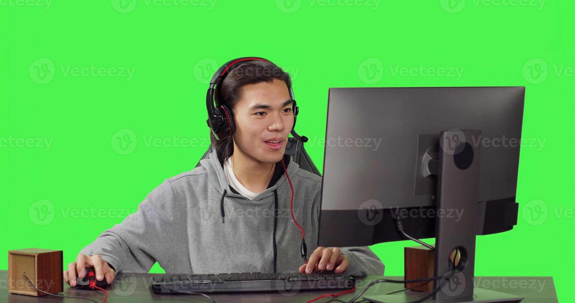 Young person sitting at desktop office, having fun with friends while enjoying online multiplayer games with headphones. Over greenscreen, asian guy competes in role playing contest. photo