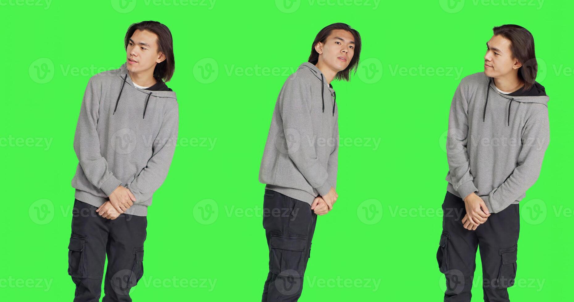 In studio, young adult poses against greenscreen backdrop, looking at wristwatch and appearing agitated. Unhappy and dissatisfied asian person is impatiently awaiting for stuff. photo