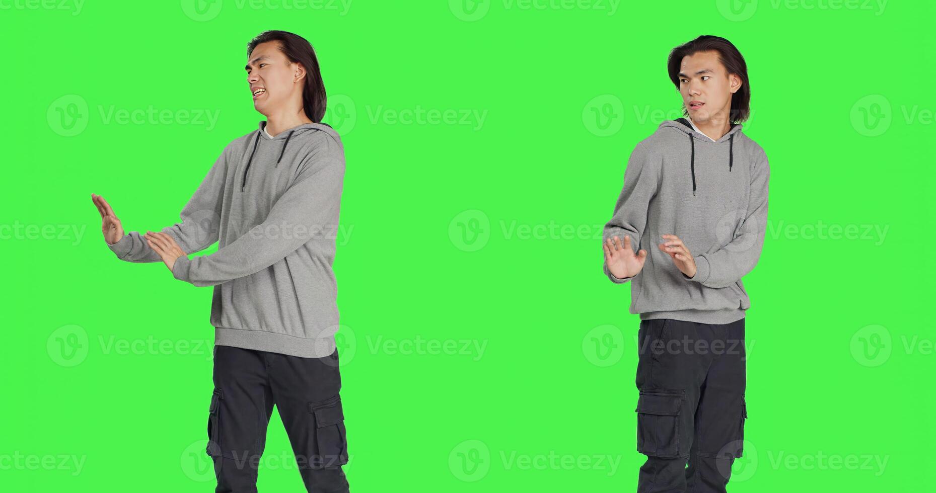 Male model pretending to push something aside, expressing rejection or refusal in studio. Young man mimicking dismissal over isolated greenscreen background, stop symbol. photo