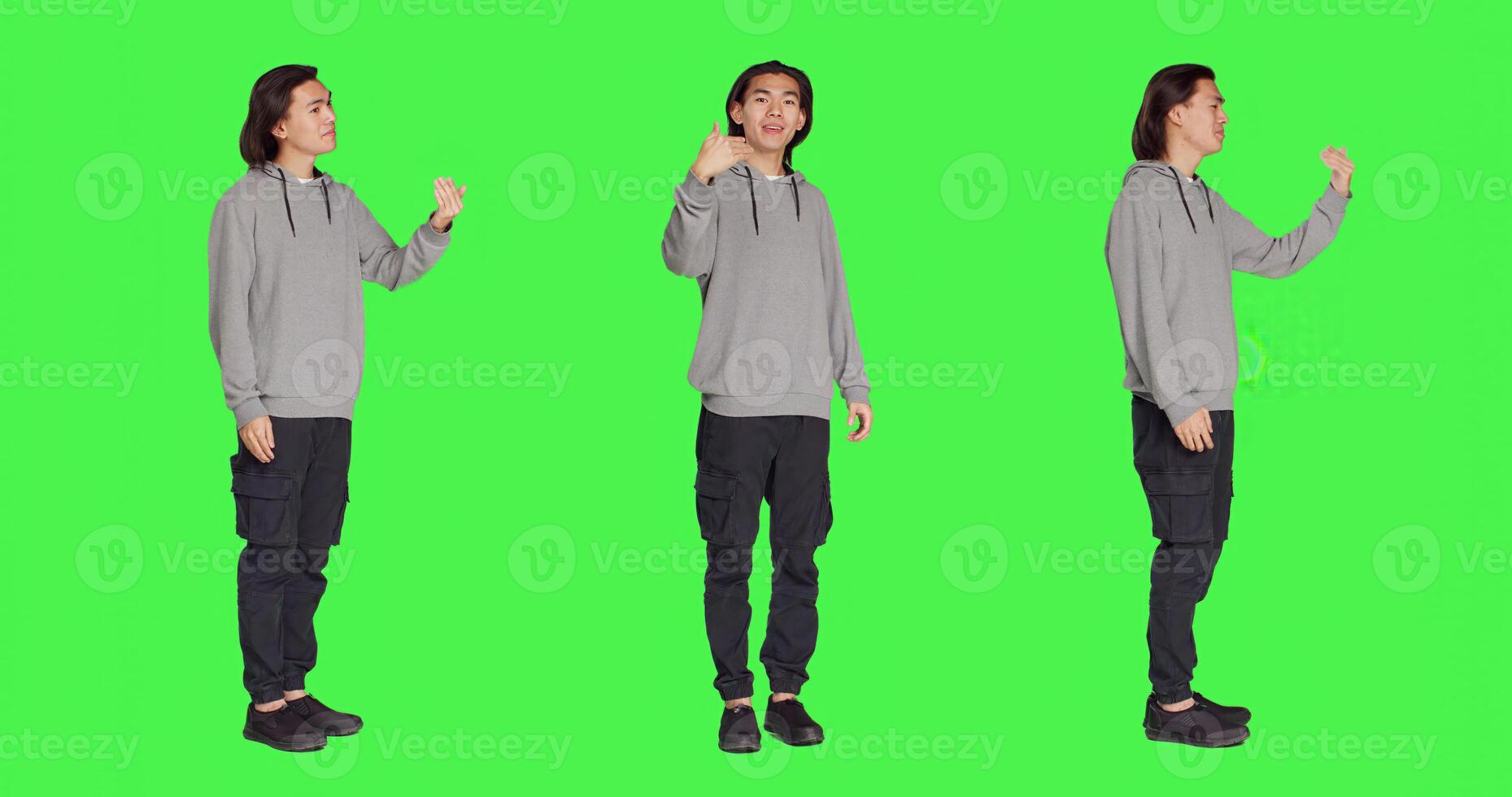 Asian man asking person to come over, encouraging people to get closer while he is standing against full body greenscreen. Adult in casual clothes urging someone to approach him. photo