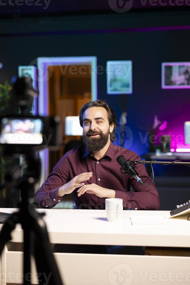 Cheerful internet star talking in front on professional camera and quality mic in studio, discussing with viewers. Joyful man using high tech recording gear to record social media video photo