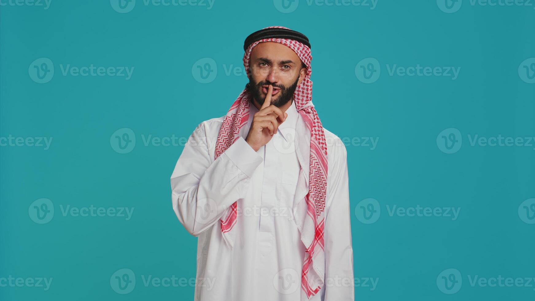 Arab man does silence sign with finger over lips, showing hush mute gesture in studio. Private model presenting confidential secrecy symbol on camera, trying to keep secret and privacy. photo