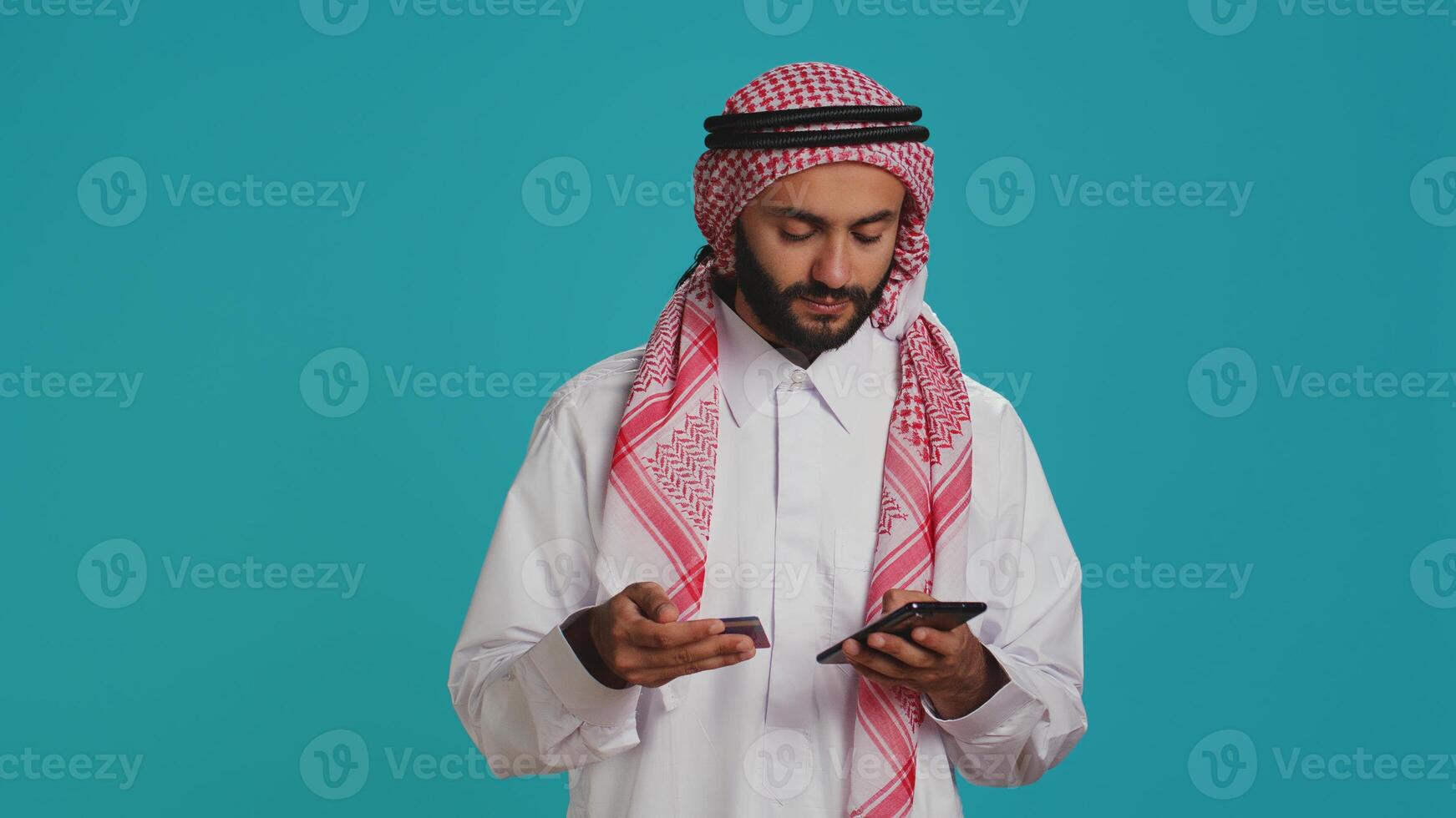 Arab person adding card numbers on website, doing online shopping spree on mall store retail app. Person paying for things on internet page, wearing traditional islamic attire with scarf. photo