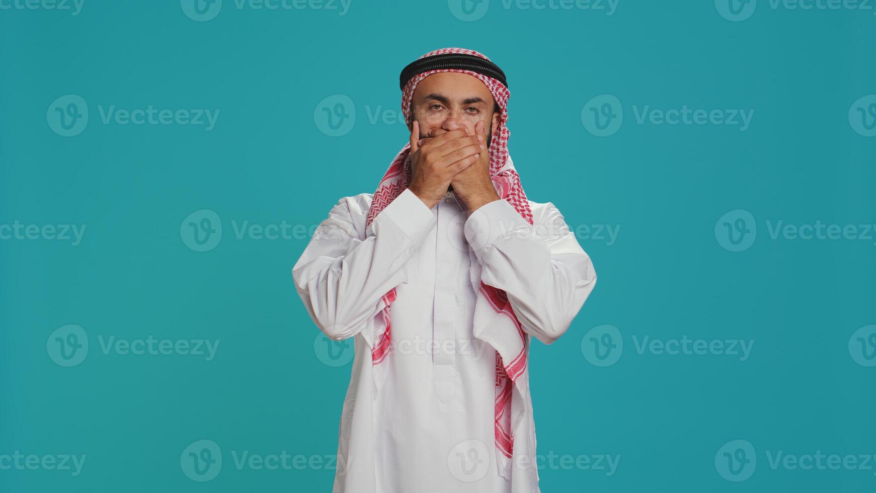 Muslim adult covers eyes, ears and mouth in studio, showcasing three wise monkeys metaphor sign. Middle eastern guy presenting dont hear, see or speak concept symbol in arabic clothes. photo