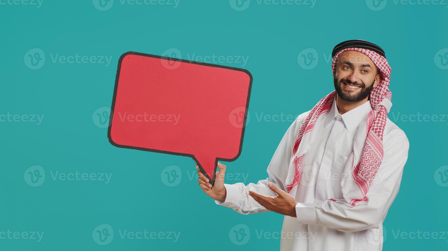 Arab person showing speech bubble in studio, creating advertisement for new commercial. Young adult working on new marketing slogan with isolated billboard icon, cardboard sign. photo