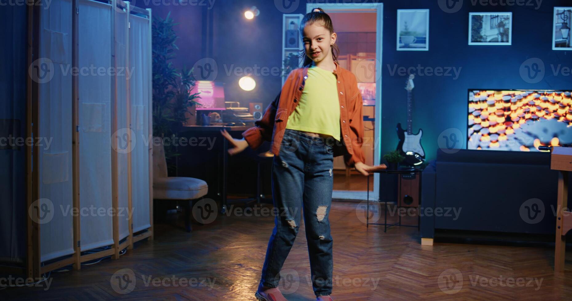 Zoom out shot of energetic child dancing and singing while shooting video for social media platform in living room. Young media star entertaining gen Z followers with professional choreography photo