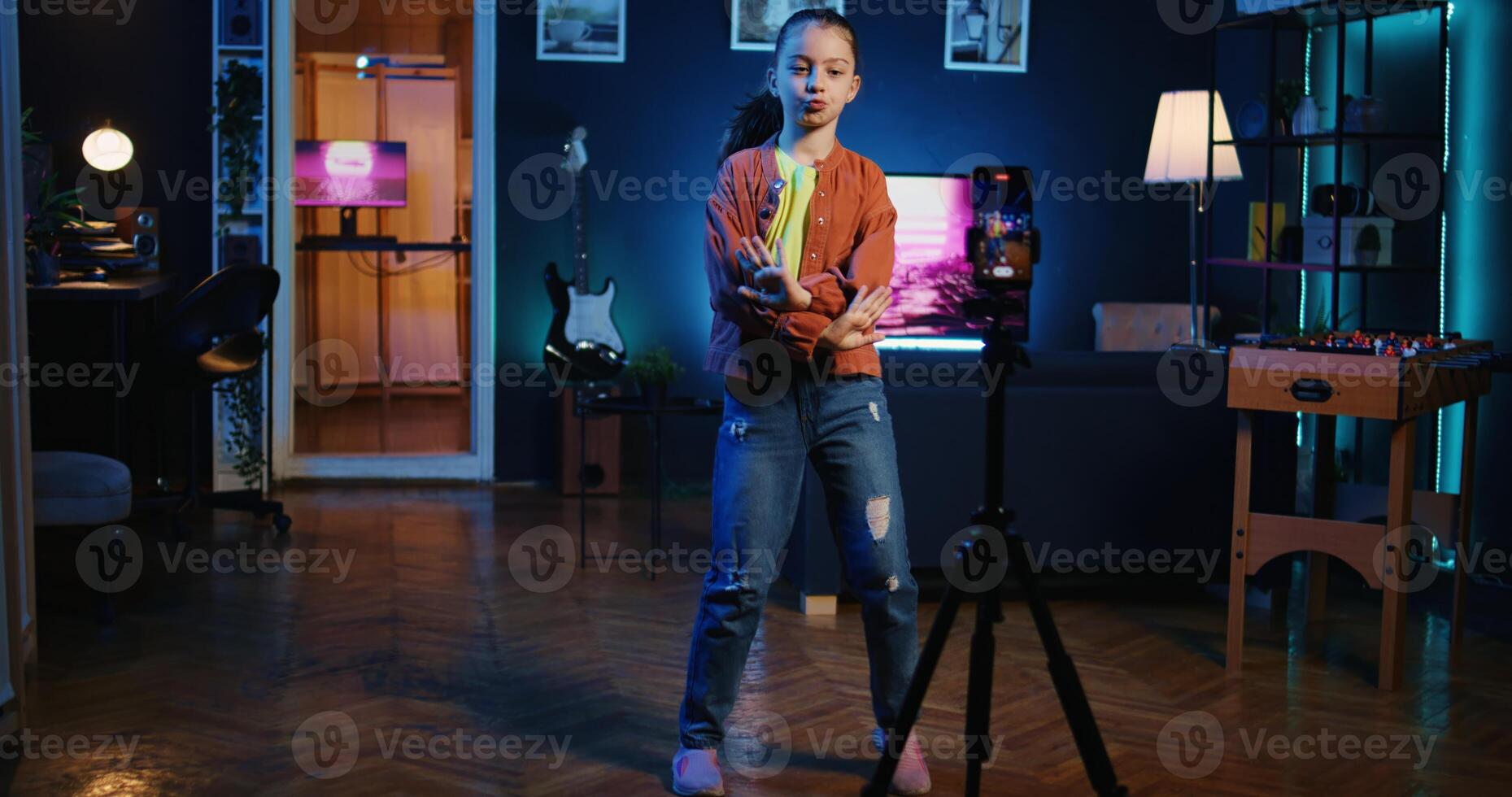 Panning shot of viral media star dancing in apartment, recording video with phone on tripod for gen z internet fans. Excited little child filming herself with cellphone doing dance moves photo