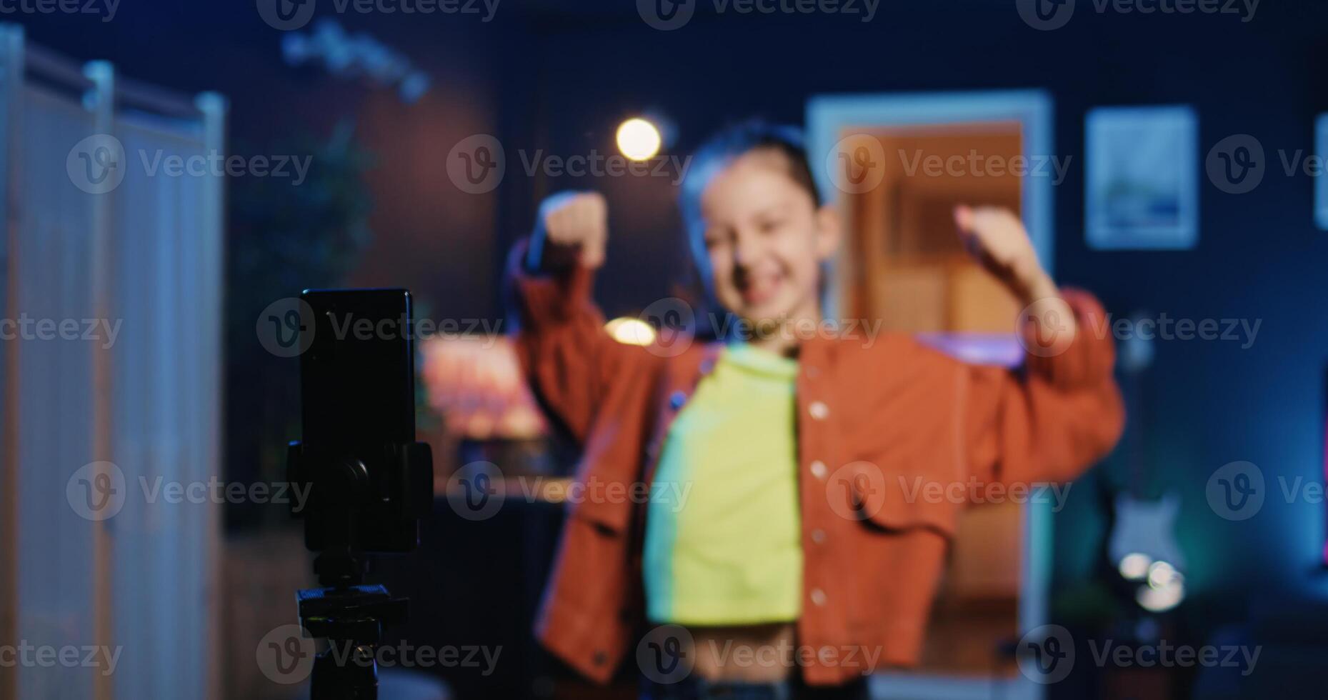 Talented kid using smartphone on tripod stabilizer to film dance tutorial for other children watching her online social media content. Merry little girl recording video targeting generation Z viewers photo