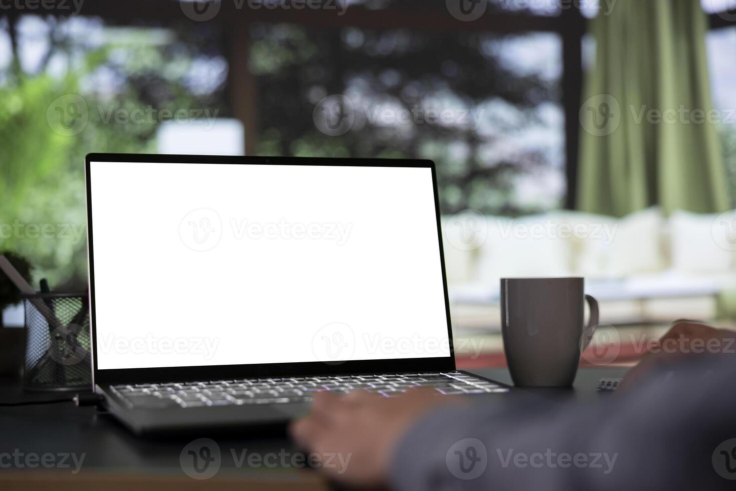 Wealthy shareholder relaxes in his posh mountain chalet and looking at white screen template on notebook. Foreign chairman works with blank mockup display on laptop from luxury forest villa. photo