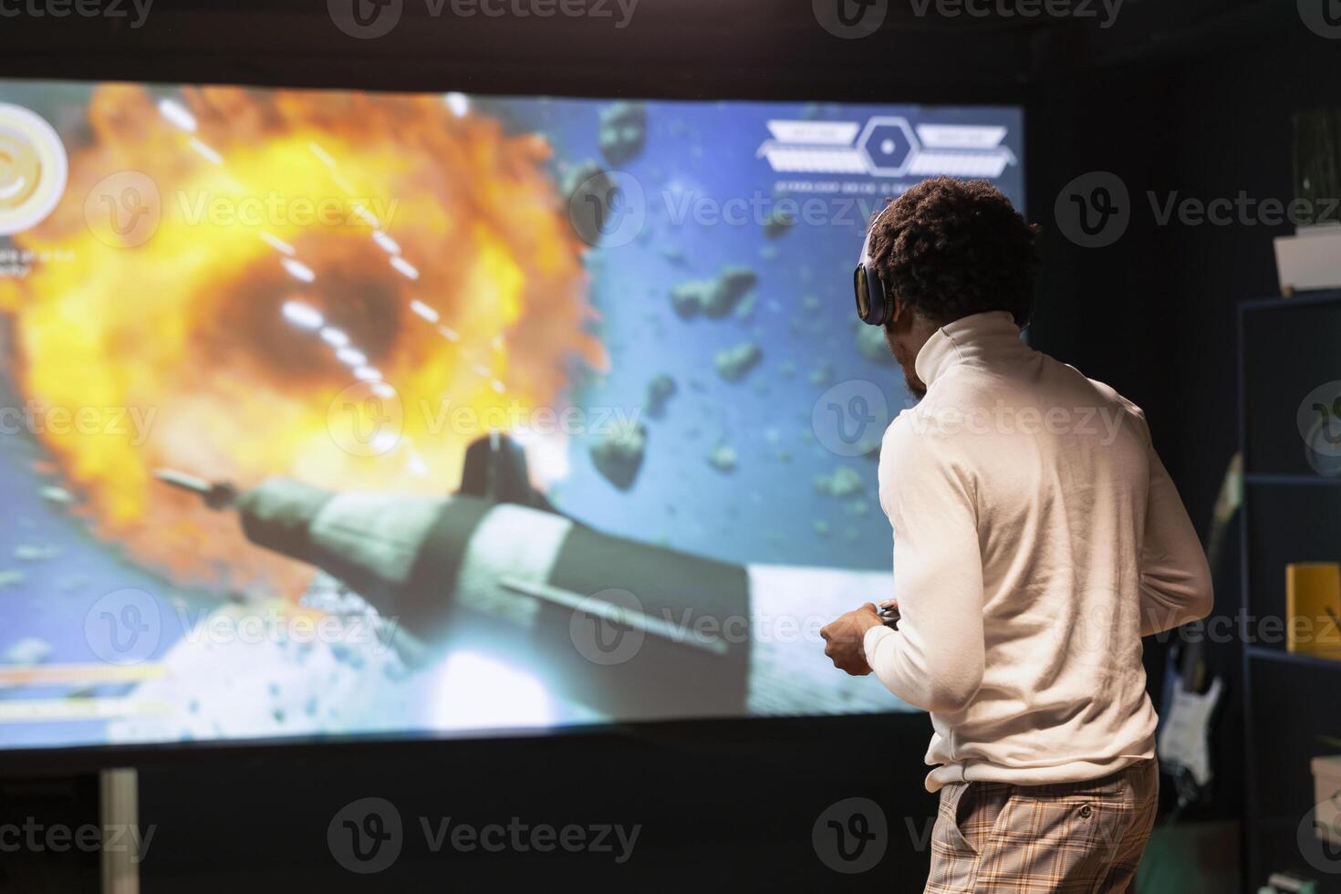 Gamer at home gaming and enjoying leisure time using high quality projector to display gameplay. Man standing up in front of ultrawide screen, playing videogame using controller photo