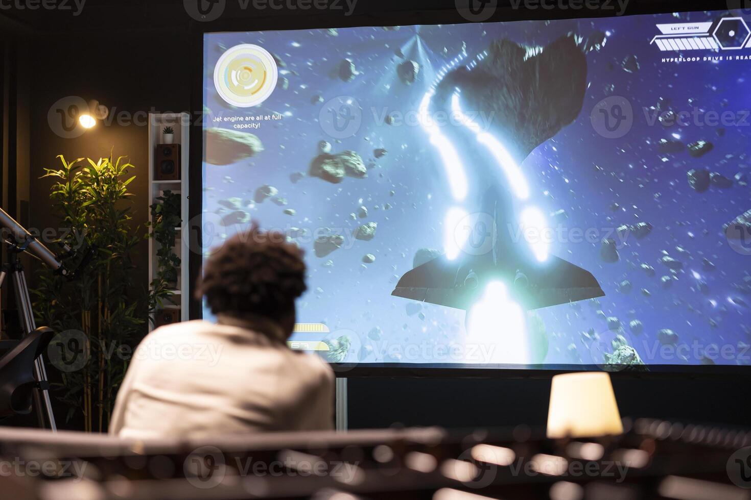 BIPOC man plays science fiction singleplayer game with overlay HUD showing health bars and minimap on huge TV screen. Player enjoying high quality ray tracing graphics in console videogame photo