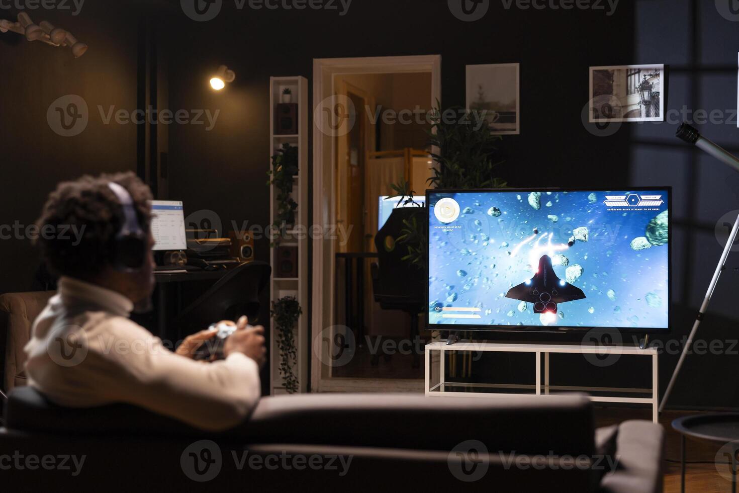 bipoc jugador jugando clásico arcada acción videojuego, volador mediante espacio escombros. hombre disfrutando ocio hora a hogar utilizando alto tecnología juego de azar consola a resolver misiones en un solo jugador juego foto