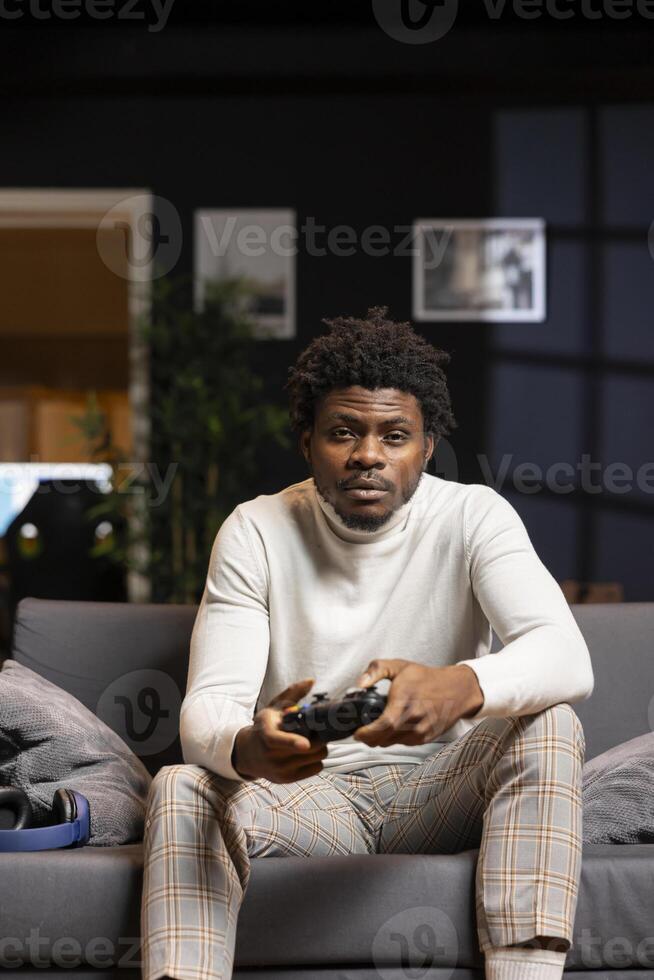 Portrait of man playing boring videogame on gaming console, feeling turned off by uninteresting levels. Gamer at home disappointed by game, struggling to maintain interest, using joystick controller photo