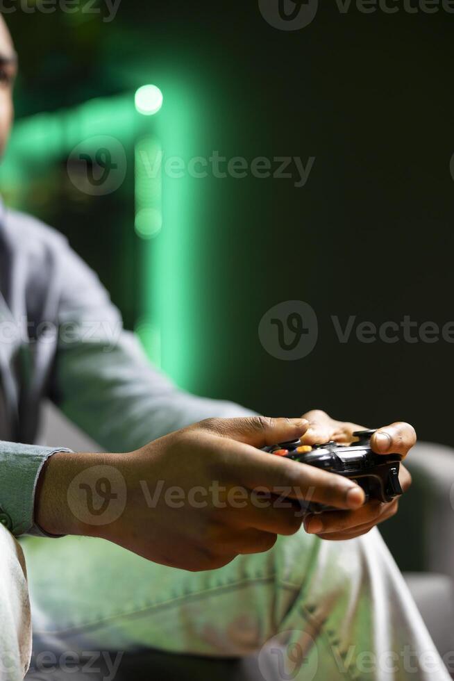 Gamer on couch using controller and headphones to play videogame in neon lit apartment, close up. Player in RGB illuminated living room using high tech gaming console joystick photo