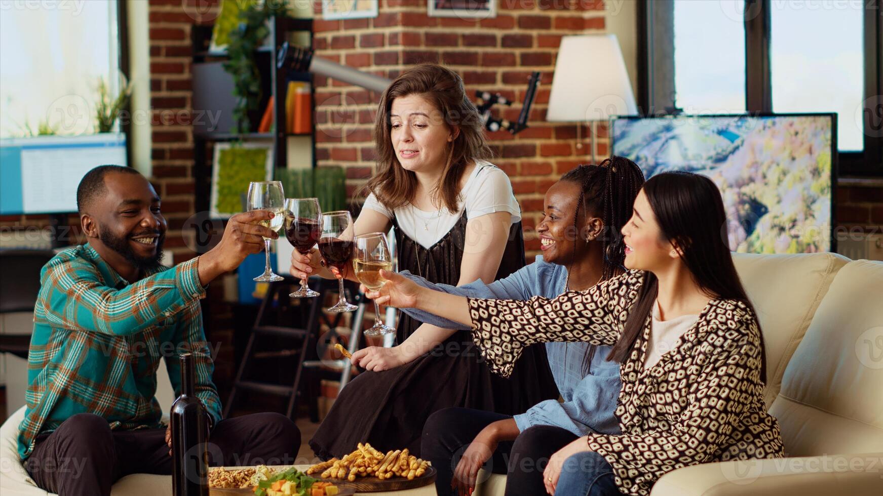 Multiracial group of people celebrating their friendship together, toasting wine and champagne glasses at home party. Joyful friends having reunion gathering, enjoying alcoholic drinks photo