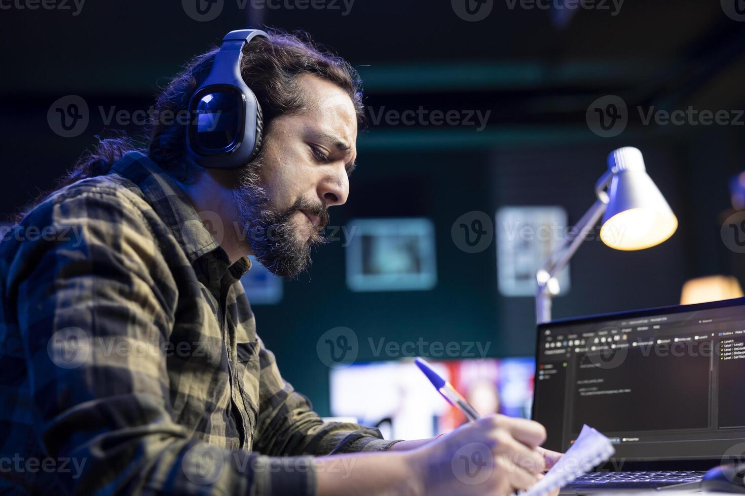 Focused man with headset, managing software and programming code on laptop. Skilled male programmer grasping notebook, providing online services, and maintaining network security on electronic device. photo