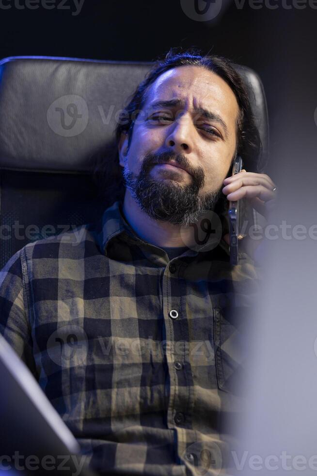 Portrait of young man sitting and having a conversation on his smartphone. Closeup of male individual with a confused facial expression, talking on his mobile device. photo