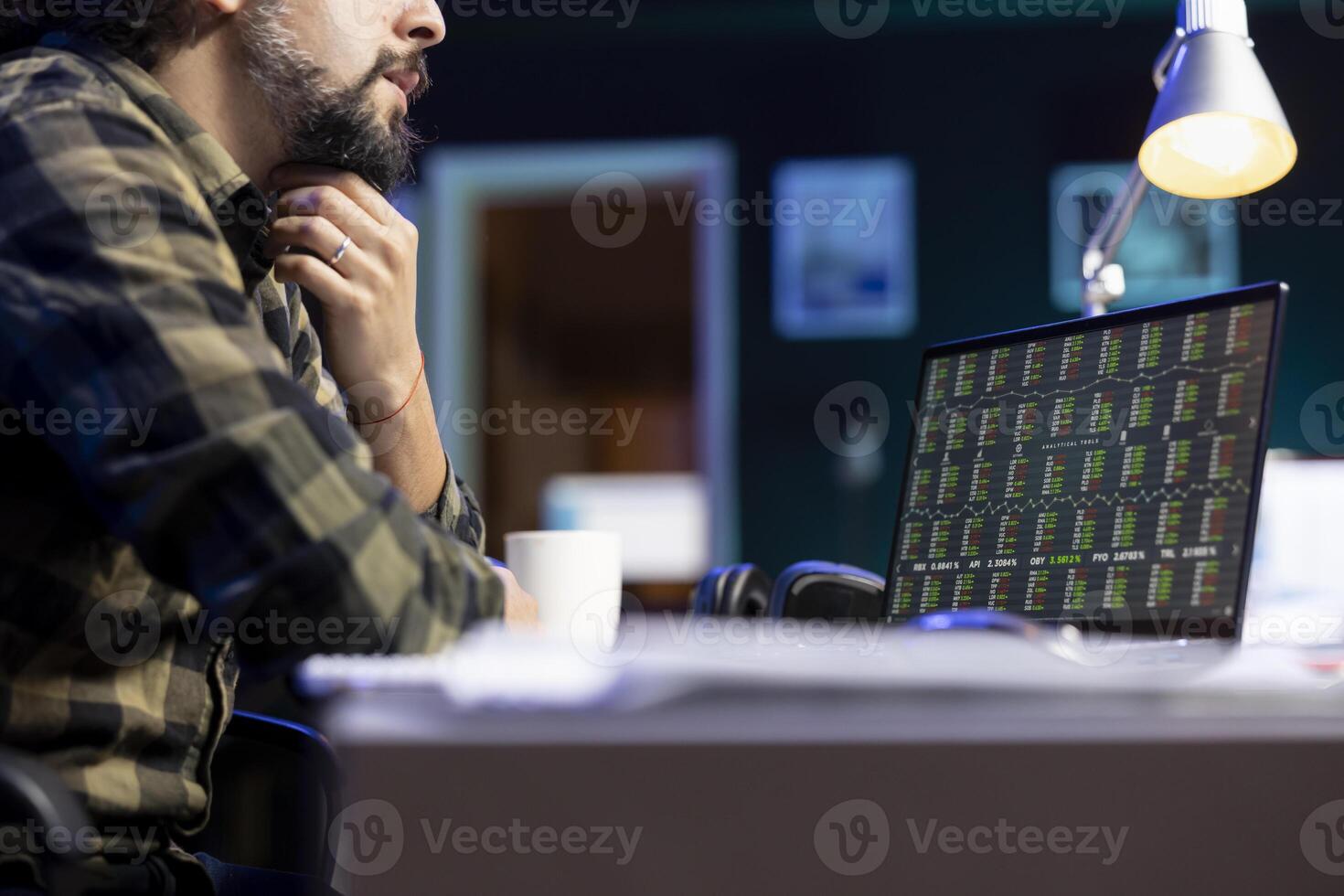 Image showing bearded man checking economic financial information on his personal computer. Male individual with hand on chin, looking at laptop screen displaying stock market. photo