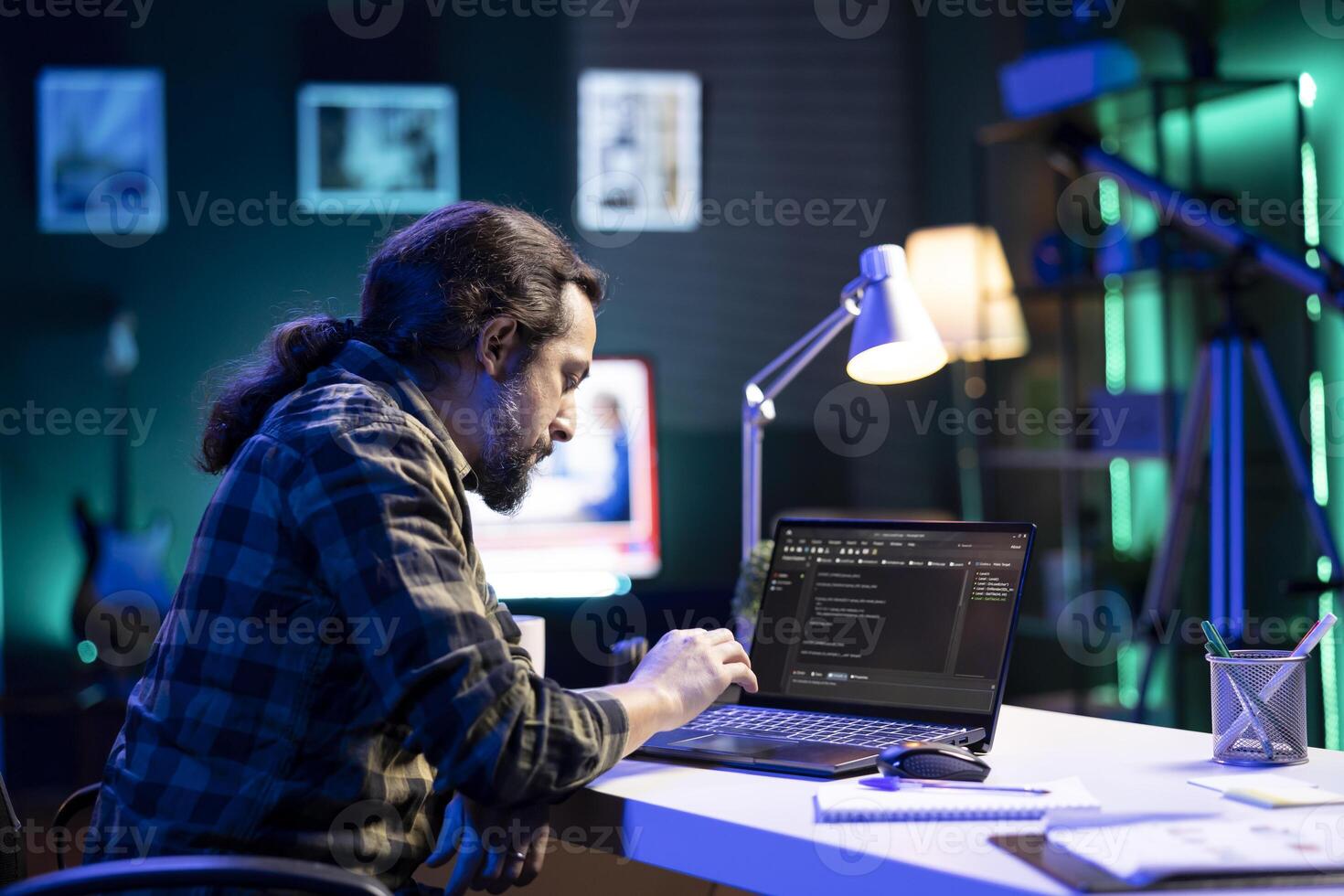 Dedicated male programmer uses his portable computer to manage databases and keep an eye on network security. Bearded man is coding on a digital laptop while seated at a desk. photo