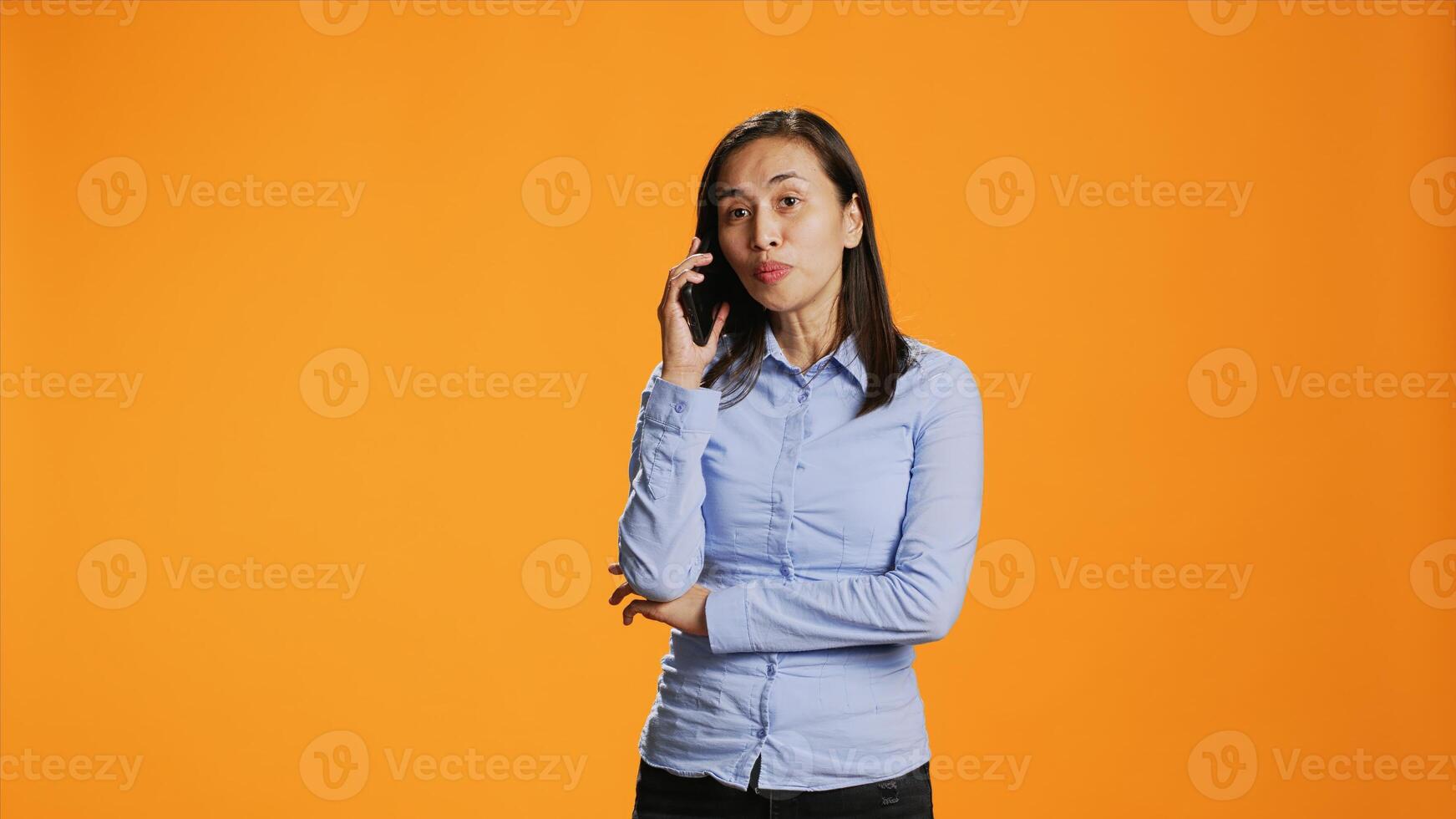 Relaxed person accepting calls in front of the lens interacting with friends on mobile telecoms connection. In the studio, asian girl answers smartphone for remote conversation, chatting. photo