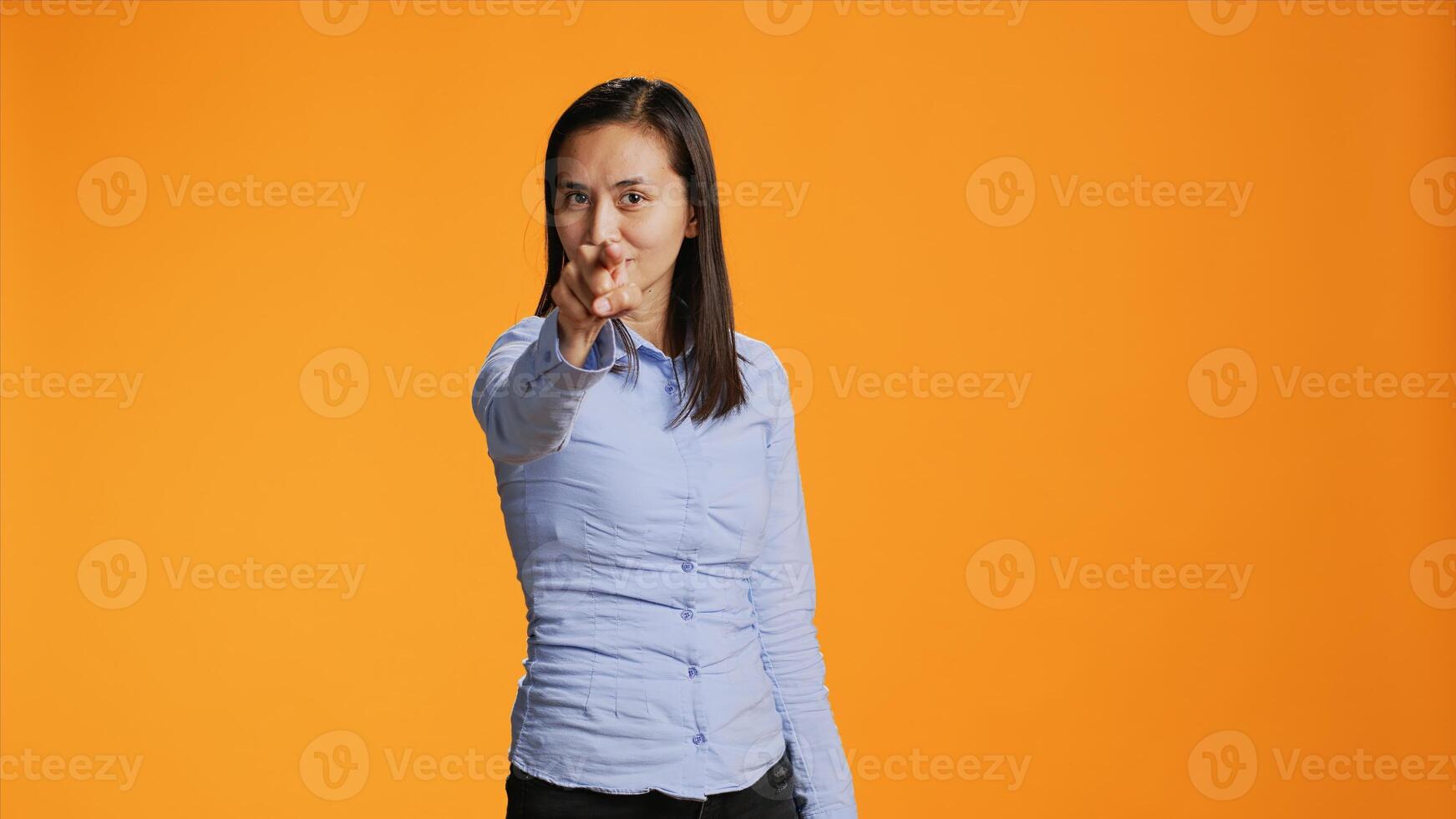 Asian model pointing at the camera in colorful studio, looking into the lens with confidence. Young filipino woman points index finger and standing proud against orange background. photo